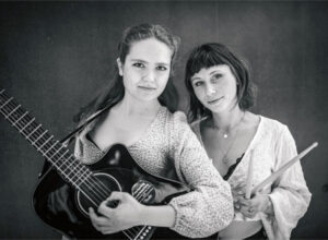 Photo en noir et blanc des deux membres originelles du groupe Herschel : Marta avec sa guitare et Camille avec ses baguettes de batterie.