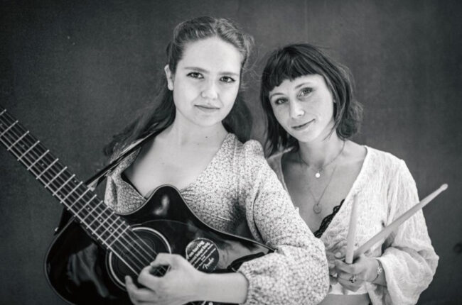 Photo en noir et blanc des deux membres originelles du groupe Herschel : Marta avec sa guitare et Camille avec ses baguettes de batterie.
